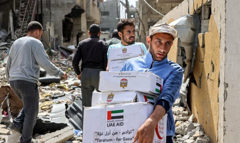 Des hommes marchent au milieu des décombres de bâtiments en portant des colis d'aide humanitaire largués au-dessus du nord de la bande de Gaza, le 23 avril 2024