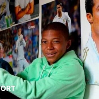 Kylian Mbappe sits on his bed with posters of Real Madrid's Cristiano Ronaldo all around him