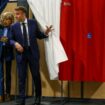 Le président français Emmanuel Macron (à droite) et son épouse Brigitte Macron (à gauche) sortent d'un isoloir, orné de rideaux arborant les couleurs du drapeau français, avant de voter pour l'élection du Parlement européen dans un bureau de vote au Touquet, dans le nord de la France, le 9 juin 2024.