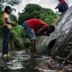 A man drinks water from a wastewater stream in a makeshift camp where migrants live at the Cavani stadium in Mamoudzou on the French island of Mayotte, on February 15, 2024. France's Minister of the Interior Gerald Darmanin announced on February 11, 2024, a constitutional amendment to eliminate "Jus Soli", the acquisition of citizenship by birth within a territory, on the Indian Ocean island of Mayotte, which faces an ongoing migration crisis. (Photo by JULIEN DE ROSA / AFP)