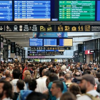 Des passagers se rassemblent autour des tableaux des départs et des arrivées à la gare Montparnasse à Paris, le 26 juillet 2024, après des actes de "sabotage" de grande ampleur.