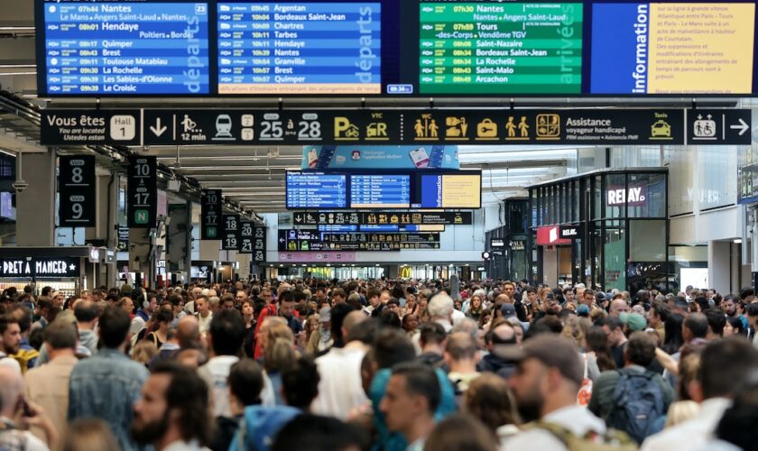 Des passagers se rassemblent autour des tableaux des départs et des arrivées à la gare Montparnasse à Paris, le 26 juillet 2024, après des actes de "sabotage" de grande ampleur.