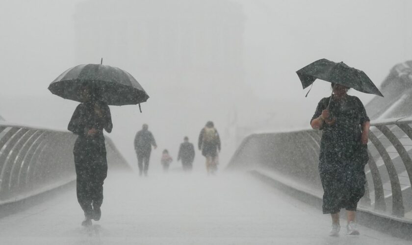 People with umbrellas walking in the rain on Millennium Bridge, London. After weeks of sweltering weather, which has caused drought and left land parched, the Met Office's yellow thunderstorm warning forecasts torrential rain and thunderstorms that c