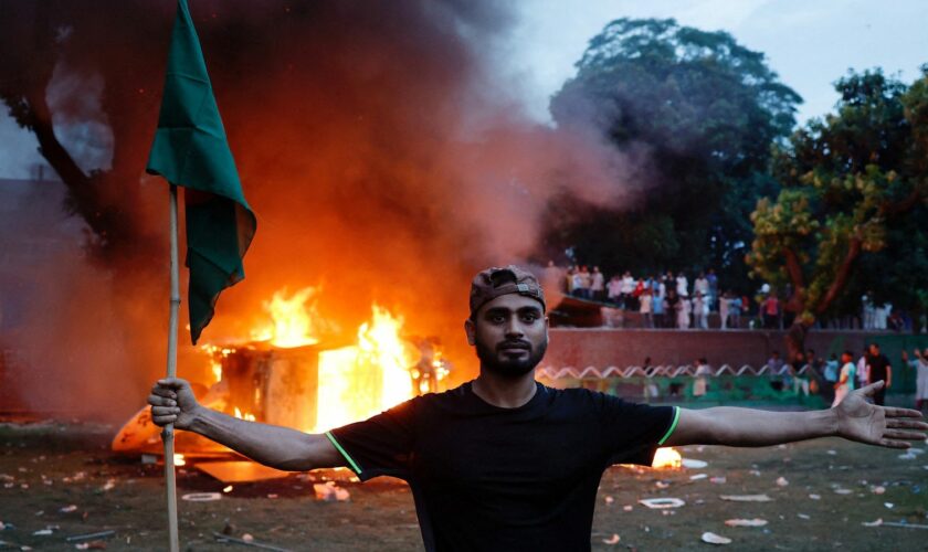 A man holding a Bangladesh flag stands in front of a vehicle that was set on fire at the Ganabhaban, the Prime Minister's residence, after the resignation of PM Sheikh Hasina in Dhaka, Bangladesh, August 5, 2024. REUTERS/Mohammad Ponir Hossain TPX IMAGES OF THE DAY