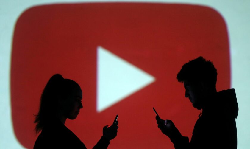 Silhouettes of mobile users are seen next to a screen projection of Youtube logo in this picture illustration taken March 28, 2018. REUTERS/Dado Ruvic/Illustration