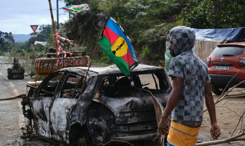 Un manifestant indépendantiste kanak près d'un véhicule calciné portant un drapeau du FLNKS lors d'un barrage routier à Houaïlou, sur la côte est de la Nouvelle-Calédonie, le 1er juillet 2024