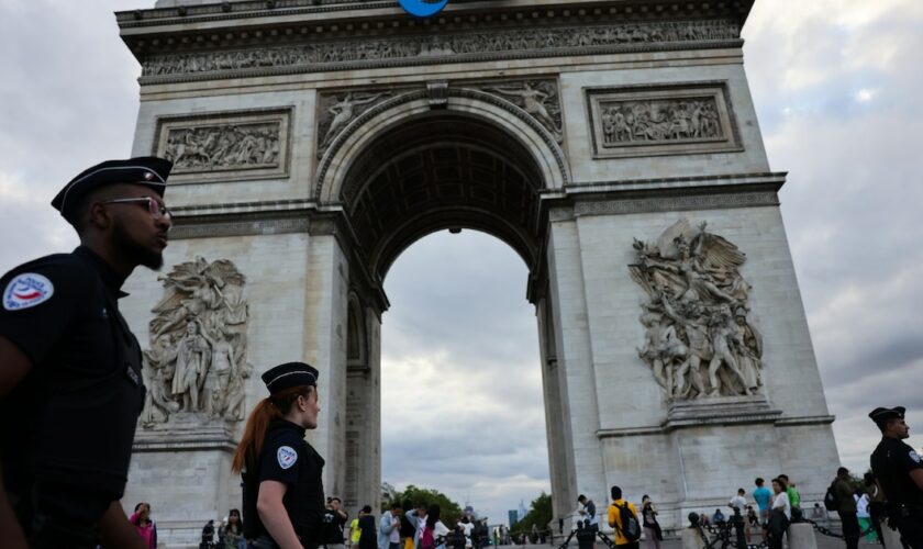 Des policiers passent devant l'Arc de triomphe arborant le sigle des Jeux paralympiques de Paris, le 22 juillet 2024