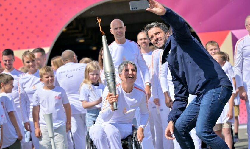 Le président du Comité d'organisation des Jeux (Cojo) Tony Estanguet (D) prend un selfie avec Emmanuelle Assmann porteuse de la flamme paralympique, le 25 août 2024 à Coquelles dans le Pas-de-Calais