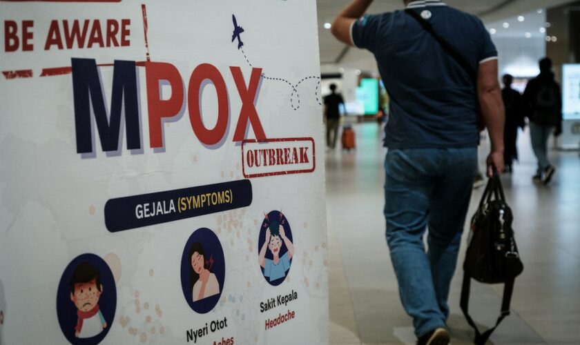 Un passager passe devant une bannière informant sur la variole du singe (MPOX) à l'aéroport international Soekarno-Hatta de Tangerang, le 26 août 2024.