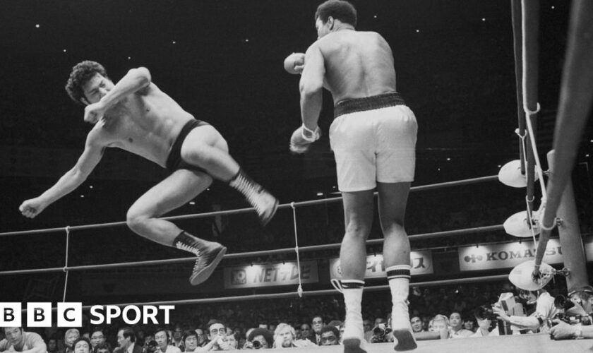 Antonio Inoki is in mid air aiming a kick at Muhammad Ali's legs.