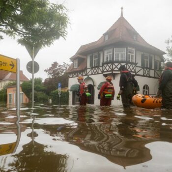 Feuerwehrleute und Wasserretter waten durch eine überflutete Straße.