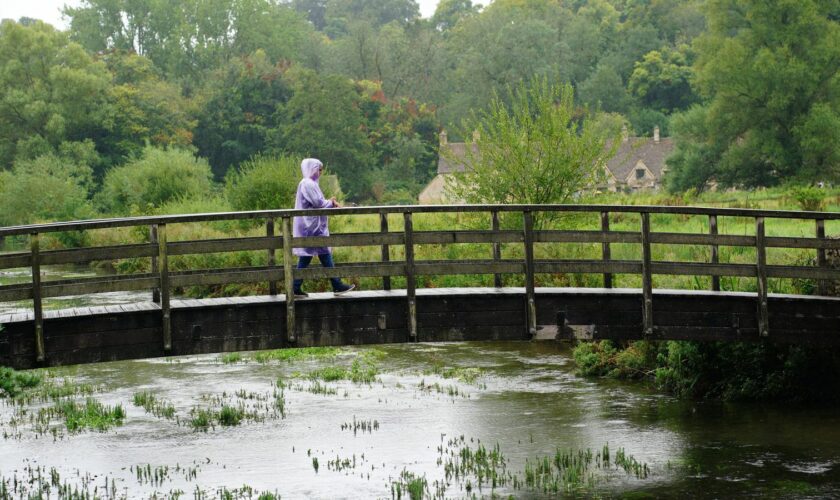 A visitor to Bibury village in Gloucestershire braves the rainy weather. Pic: PA