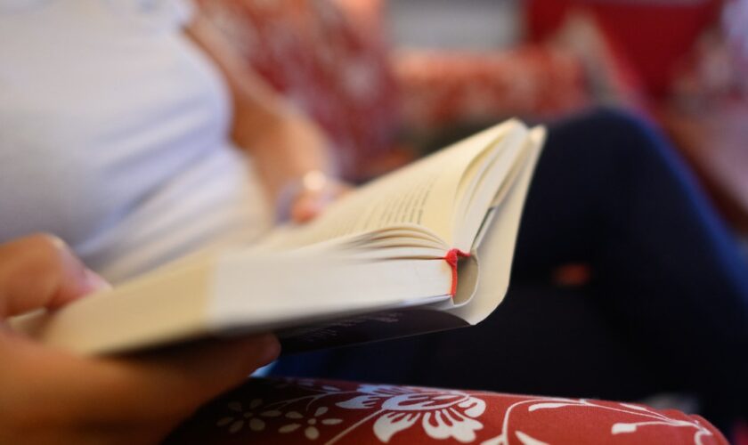 Une femme lit un livre sur un canapé.