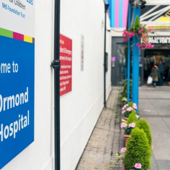 London, UK - A welcome sign outside the NHS Great Ormond Street Hospital for Children in London, with people by the entrance in the background.