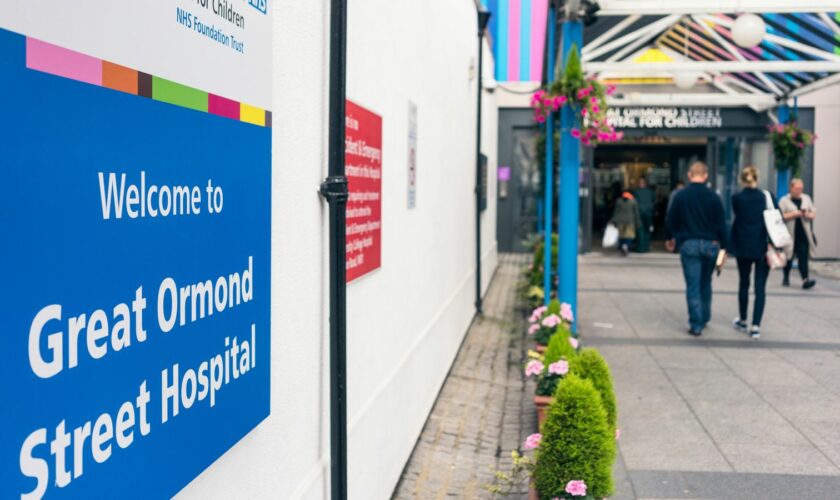 London, UK - A welcome sign outside the NHS Great Ormond Street Hospital for Children in London, with people by the entrance in the background.