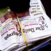 A newsagent carries a pile of Daily Telegraph newspapers