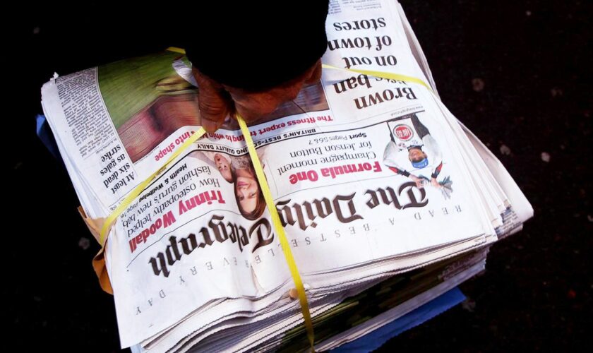 A newsagent carries a pile of Daily Telegraph newspapers