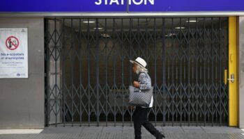 Une passante marche devant les grilles fermées de la station de métro Victoria à Londres le 19 août 2022, alors que le réseau de transports en commun de la capitale britannique est très perturbé par une grève pour les salaires face à l'inflation