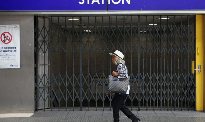 Une passante marche devant les grilles fermées de la station de métro Victoria à Londres le 19 août 2022, alors que le réseau de transports en commun de la capitale britannique est très perturbé par une grève pour les salaires face à l'inflation