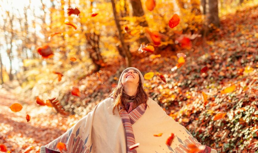 Eine Frau steht lachend unter herabfallendem Herbstlaub.