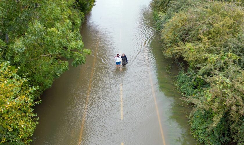 People wade along a flooded road in Offord Cluny, Cambridgeshire last week. Pic: PA