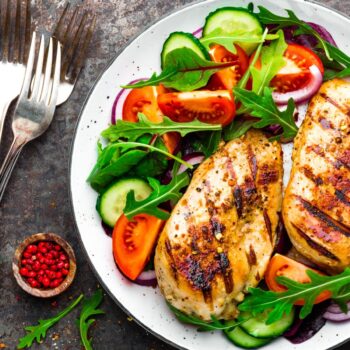 Grilled chicken breast. Fried chicken fillet and fresh vegetable salad of tomatoes, cucumbers and arugula leaves. Chicken meat with salad. Healthy food. Flat lay. Top view. Dark background