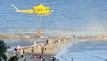 La extinción de un incendio en el Castillo de Santa Bárbara de Alicante con un helicóptero cargando agua en la playa