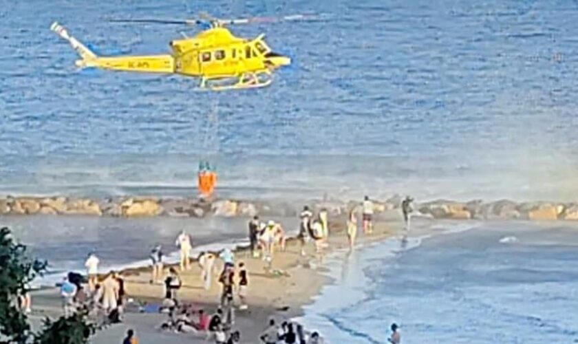 La extinción de un incendio en el Castillo de Santa Bárbara de Alicante con un helicóptero cargando agua en la playa