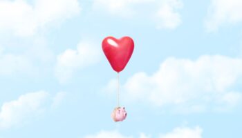 Symbolbild Finanzen in der Beziehung: Ein Sparschwein schwebt im Himmel, es ist an einen Herz-Luftballon gebunden