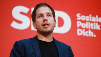 Kevin Kühnert spricht vor einer roten Wand mit weißem Logo der SPD