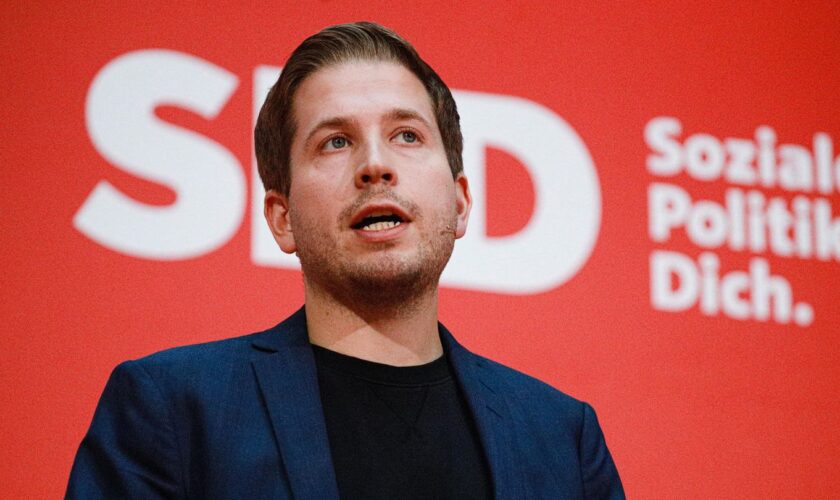 Kevin Kühnert spricht vor einer roten Wand mit weißem Logo der SPD