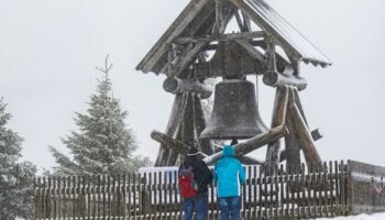 Zwei Wanderer stehen vor der Friedensglocke auf dem Fichtelberg. (Archivbild) Foto: Kristin Schmidt/dpa-Zentralbild/dpa