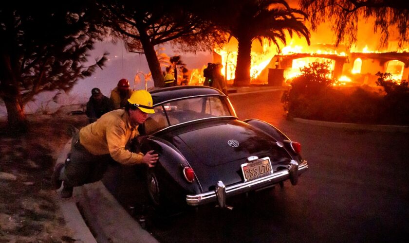 Firefighters and sheriff's deputies push a vintage car away from a burning home as the Mountain Fire burns in Camarillo, Calif., on Wednesday, Nov. 6, 2024. (AP Photo/Noah Berger)