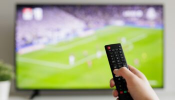 Close up of hand with remote controller and tv with football on background