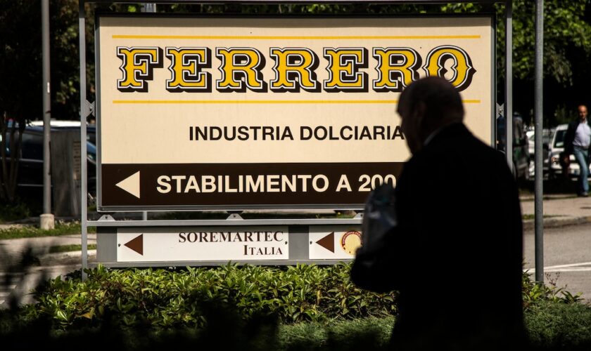 Cette photo prix le 29 mai 2019 à Alba montre un homme marchant près du logo du fabricant italien de chocolat de marque Ferrero.