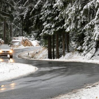 Ein Auto fährt auf einer nassen Straße durch einen Wald voller Schnee