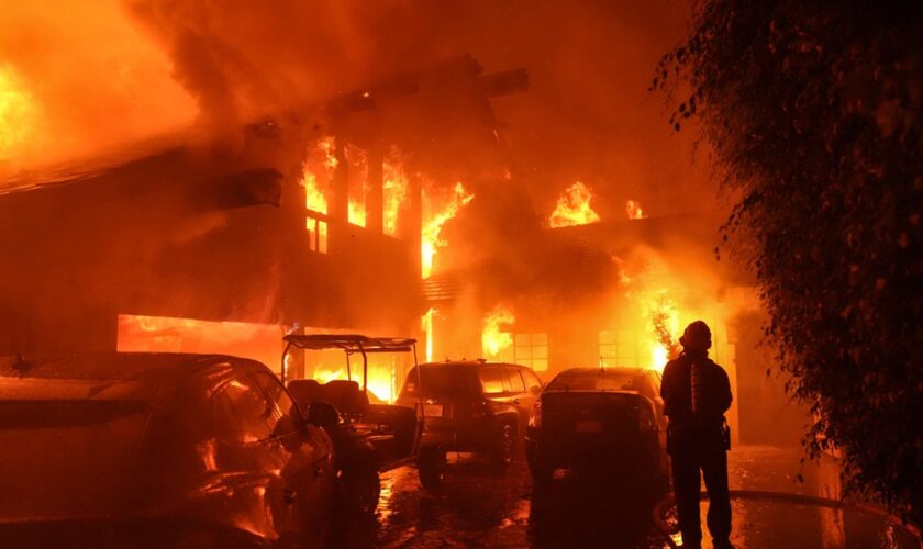 A firefighter sprays water on a home as it burns in the Franklin Fire in Malibu, California., Tuesday, Dec. 10, 2024. (AP Photo/Jae C. Hong)