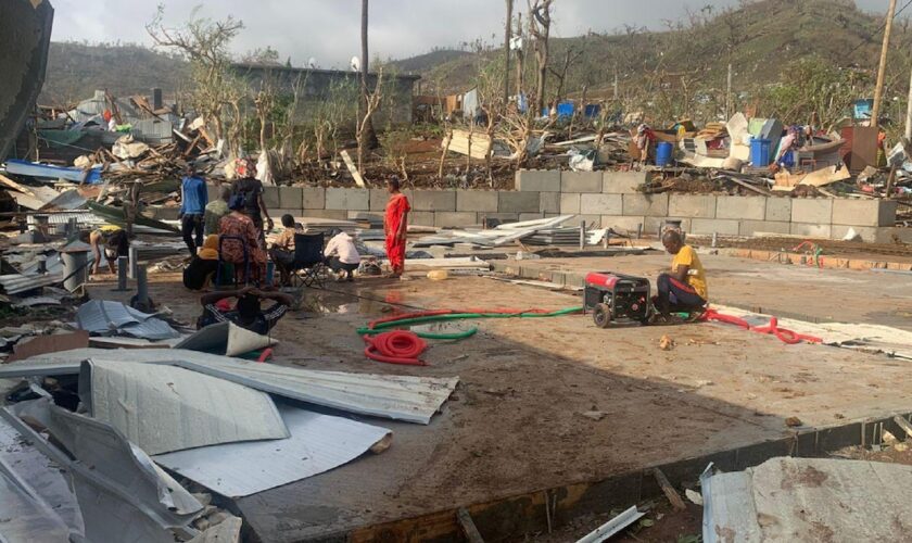 Des habitants assis au milieu de tas de débris de tôles et de bois après la destruction de leurs maisons par le cyclone Chido qui a frappé Mayotte, le 15 décembre 2024