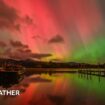 Sky filled with green and purple of the aurora with some shafts of white light running vertically. In the distance a ruined castle sits on top of a hill