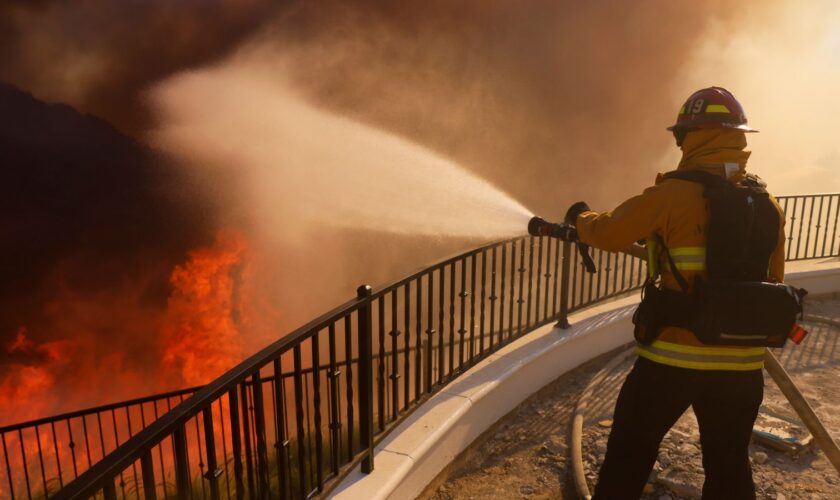 A firefighter makes a stand in front of the advancing Palisades Fire in the Pacific Palisades neighborhood of Los Angeles, Tuesday, Jan. 7, 2025. (AP Photo/Etienne Laurent)