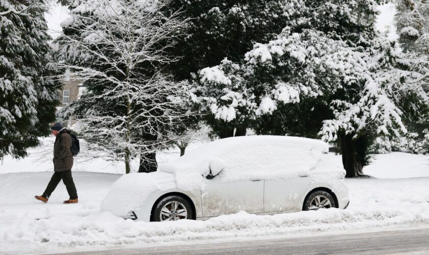 A man walks past a snow-covered car on a road in Buxton, Derbyshire, on 8 January 2025. Pic: Reuters