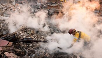 A firefighter clears away smoking debris at the site of building in Altadena. Pic: AP Photo/Chris Pizzello