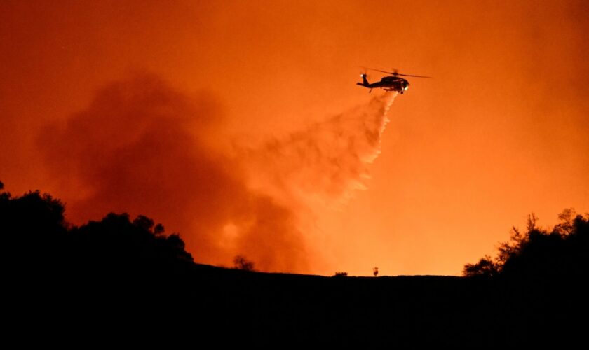 Un hélicoptère fait un largage sur des incendies en cours entre les quartiers de Mulholland drive et d'Encino, le 10 janvier 2025 à Los Angeles