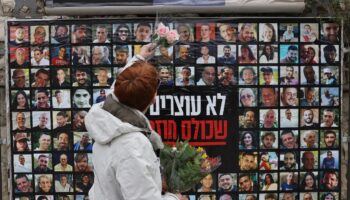 Une femme accroche une fleur sur un mur recouvert des portraits des otages israliens détenus dans la bande de Gaza, le 12 février 2024 à Jérusalem