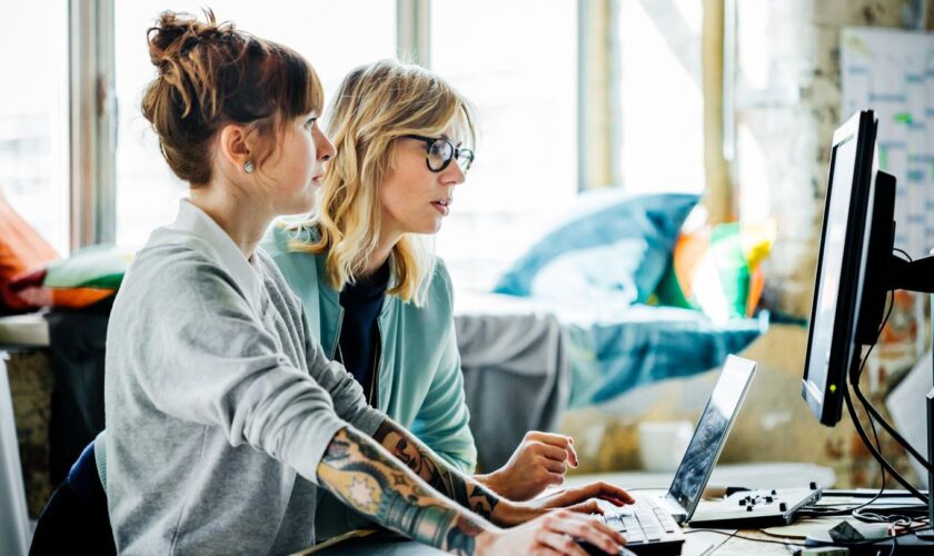 Zwei Frauen sitzen vor einem Laptop und PC-Bildschirm